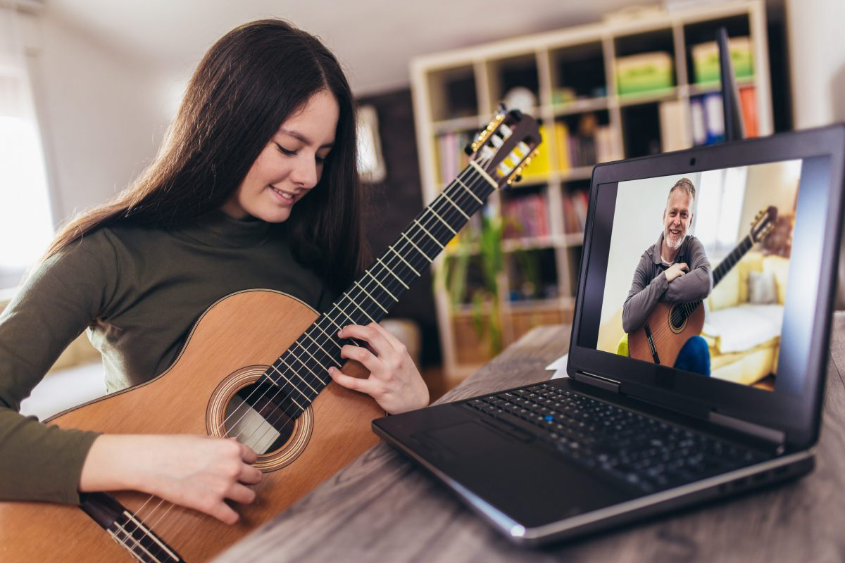 Young adult woman taking an online guitar lesson with an online guitar teacher.