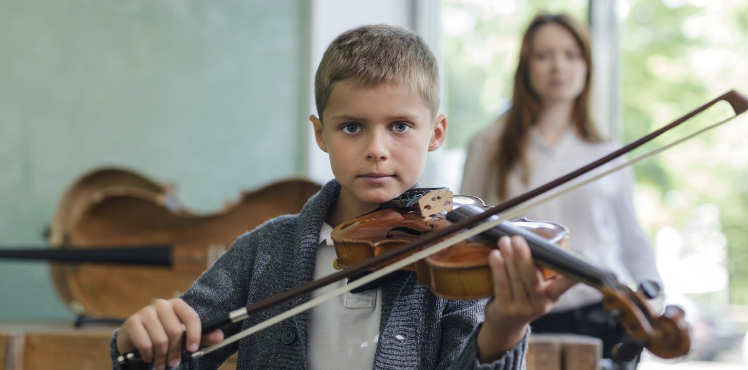 A violin student in his violin teacher's studio nearby