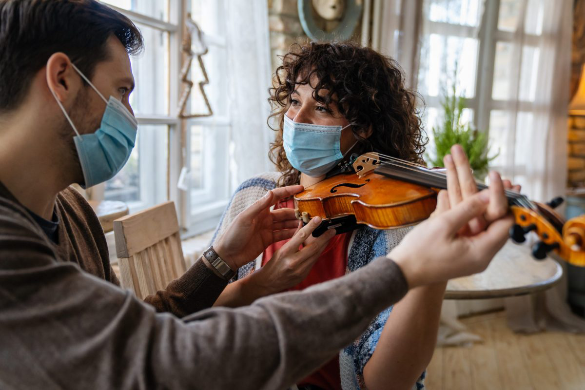 An adult violin student and teacher in a music lesson with distancing measures and masks.